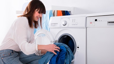 Eine junge Frau gibt Wäsche in die Waschmaschine | Bild: mauritius-images